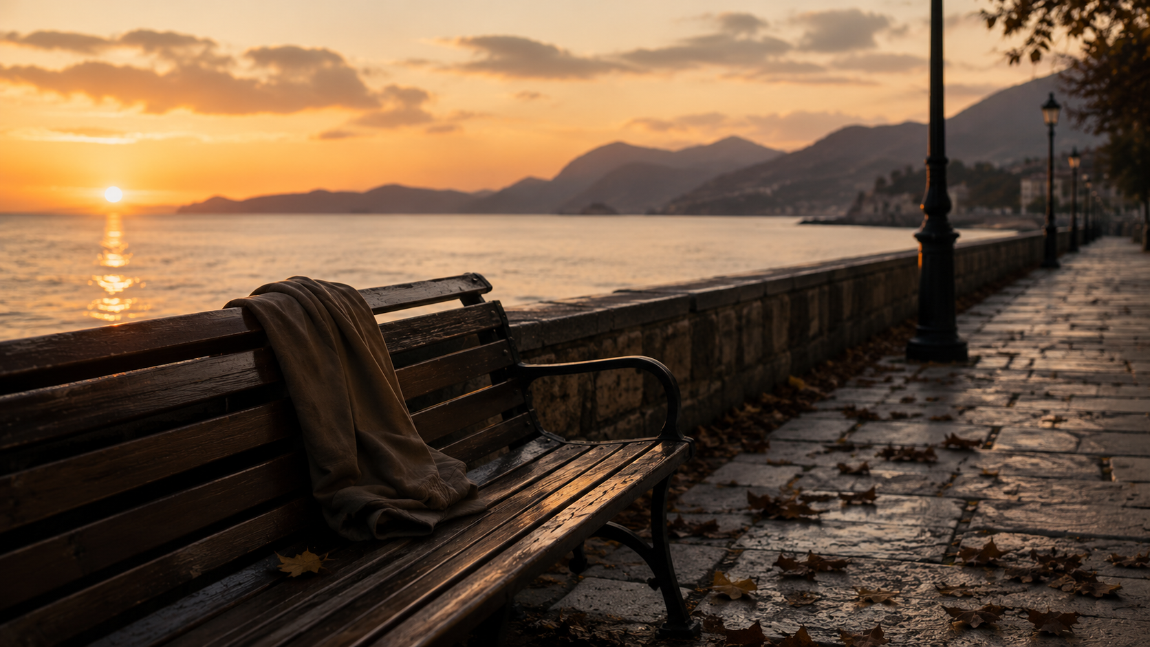 Una panchina vuota sul lungomare al tramonto, immagine della distanza tra persone che un tempo erano vicine.